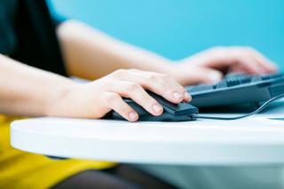 Henkilö tietokoneella, lähikuva tietokoneen näppäimistöstä, hiirestä ja käsistä.
