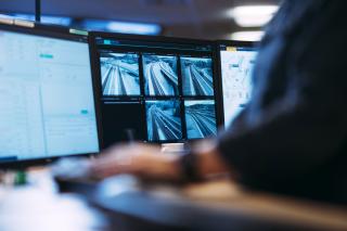 Tieliikennekeskus, jossa tieliikenneohjaajan kädet tietokoneen näppäimistöllä lähikuvassa. Taustalla monitorinäyttöjä.