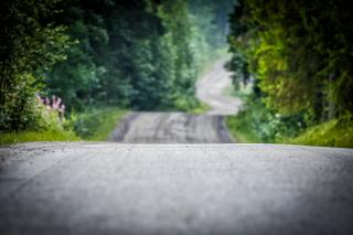 Neste Rallyn kuvituskuva, jossa mäkistä soratietä ja metsää ympärillä.
