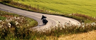 Moottoripyöräilijä ajaa kesäisessä Suomessa peltomaiseman keskellä. 