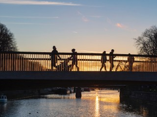 Ihmisiä ylittämässä siltaa auringon laskiessa