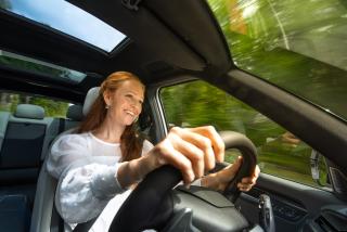 Kuvassa henkilö ajaa autolla hymyssä suin.